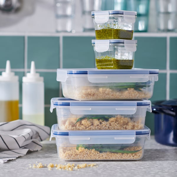 Stack of clear plastic food containers, blue seals, holding leftovers and sauce, on kitchen counter.