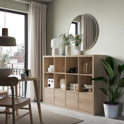Modern KALLAX shelf with dishes, vases, plant, and table.