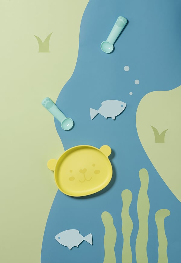 Yellow bear plate with fish, seaweed, and spoons.