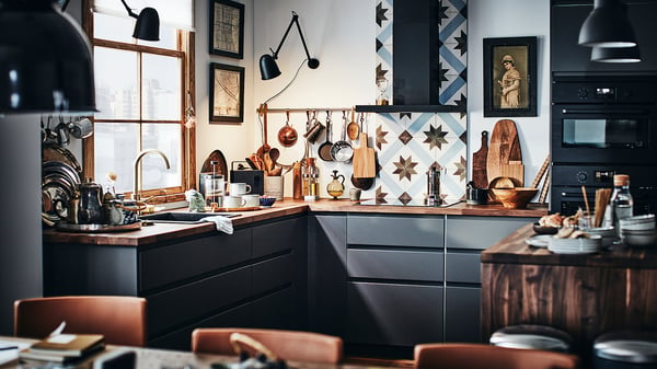 Modern kitchen with KARLBY dark wooden countertops and black cabinets. Various utensils hang above the sink. A window lets in natural light.