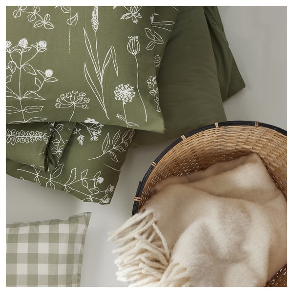 Green throw with white floral design, plush texture, woven basket with light-colored blanket, and plaid cushion.