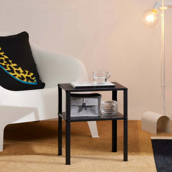 A black side table with a book, cup, and storage box on top, next to a white sofa.