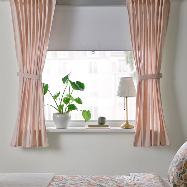 Pink LENDA curtains frame a window with a plant and lamp, set against a colourful bedspread.