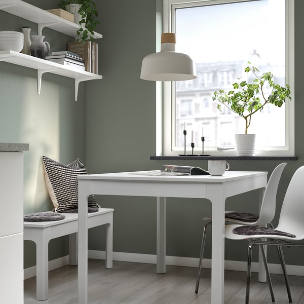 Minimalist home office with white desk, shelves, vases, books, sheepskin chairs, hanging lamp, city view.