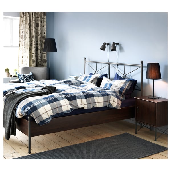 Bedroom with blue plaid bedding, wooden floor, black rug, grey wall, curtain, and modern décor.