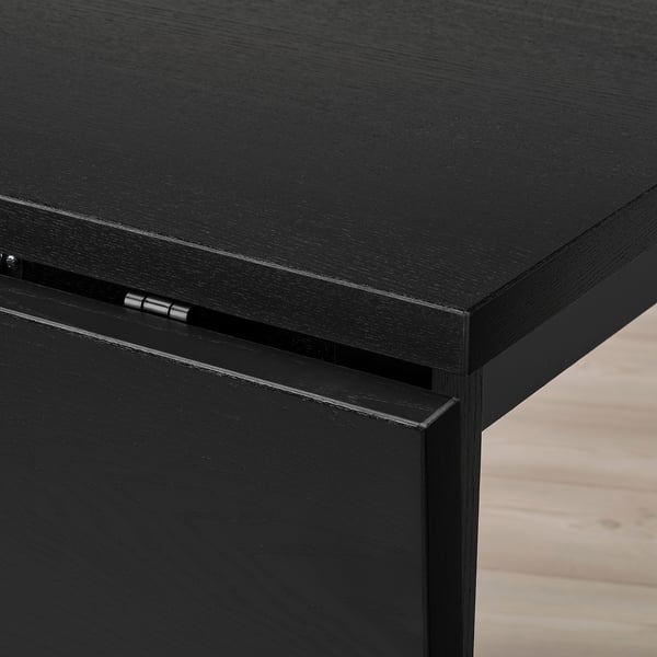 Black drop-leaf table corner detail. Sturdy, glossy finish and precise craftsmanship.