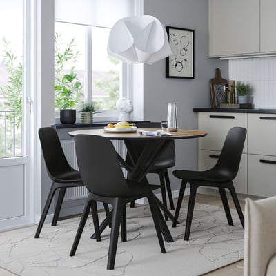 Modern dining area with NORRMJÖLE black chairs, sleek round table, geometric pendant light, and plants.