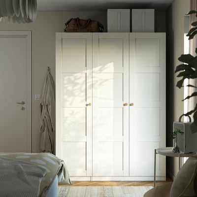 Minimalist bedroom with large white PAX wardrobe, bed, plant, and coat.