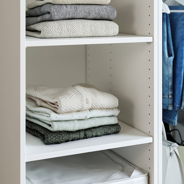 Folded clothes organised on white shelves in a closet, showcasing storage functionality.
