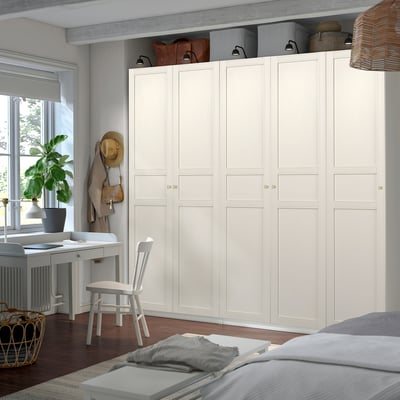 Minimalist bedroom with large white PAX wardrobe, dark floor, and small desk with plant.