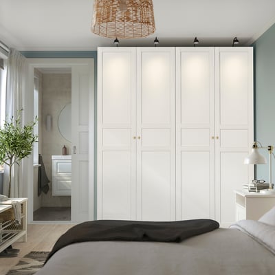 Modern bedroom with large white PAX wardrobe, gold handles, spotlights, grey bed, desk, and bathroom door.