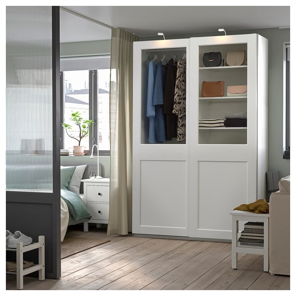 A modern white PAX wardrobe with glass doors, displaying clothes and accessories.