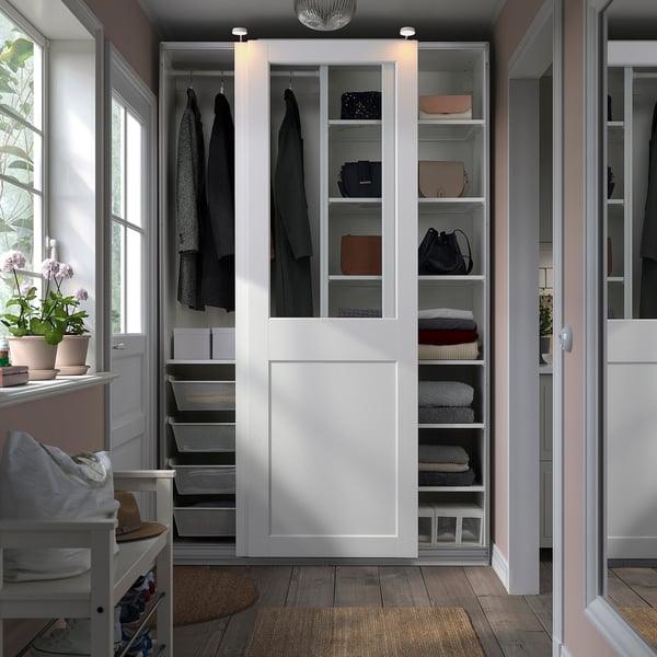 White PAX wardrobe with glass doors showing clothes, between windows with plants.