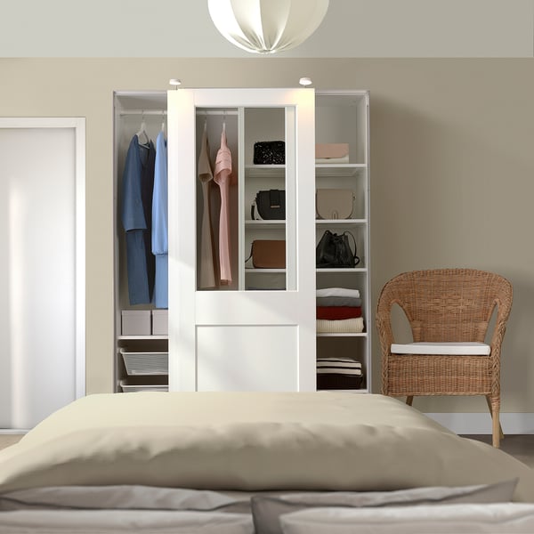 Bedroom with large white PAX wardrobe, glass/wood doors, wicker chair, beige bed.