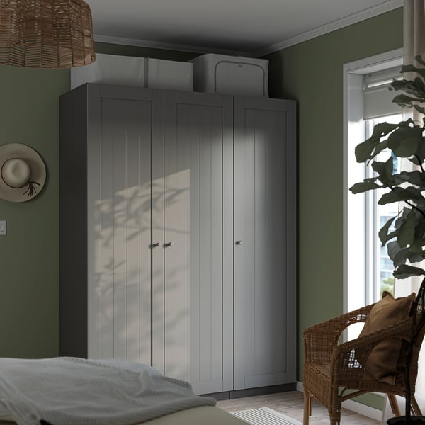Modern bedroom with tall grey PAX wardrobe, wicker chair, bed, and plant.
