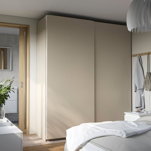 Modern beige PAX wardrobe with sliding doors fills bedroom wall, taller than white bed.