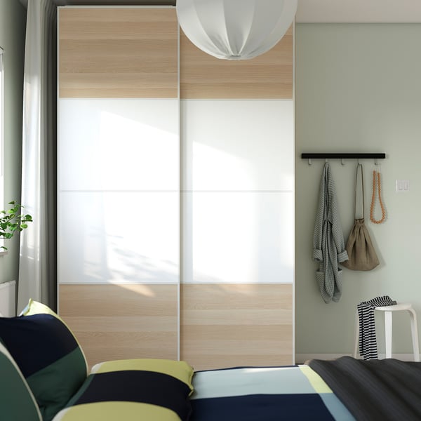 Modern bedroom with IKEA PAX wardrobe, sliding doors, coat rack, and accent chair.
