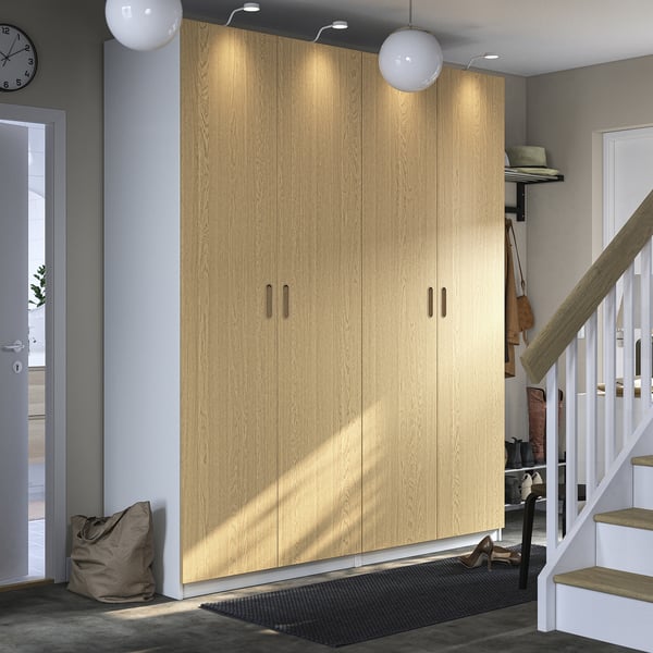 Large wooden PAX closet stands tall beside entrance, lighting accentuates natural oak finish, rectangle shape, simple modern design.