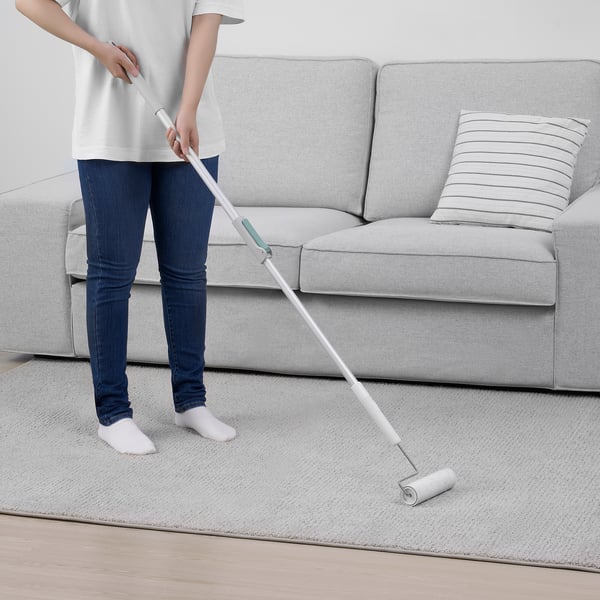 Person cleaning a carpet using a wide lint roller standing next to a couch.