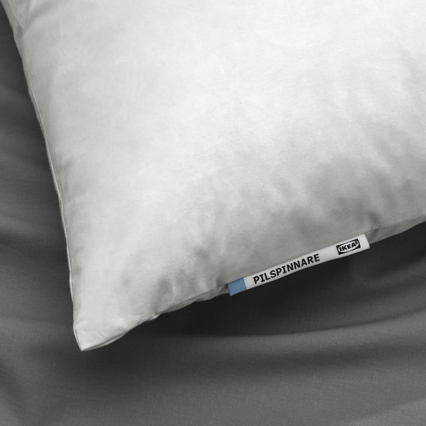 White pillow on gray bedding, branded with ikea PILSPINNARE label, showcasing feather-filled, soft cotton design for comfortable sleep.