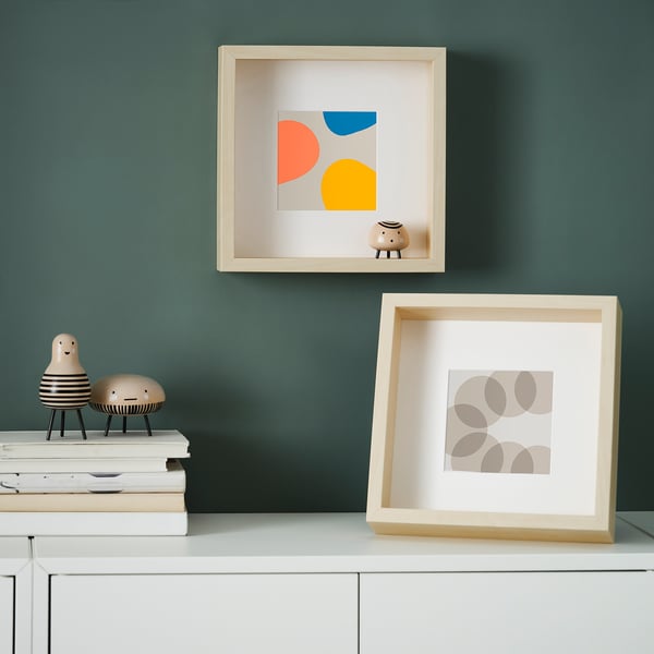 Two modern art frames displayed on a shelf against a teal wall. One is mounted on the wall, the other stands on the shelf.