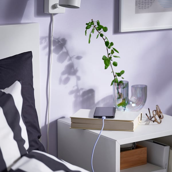 A charging cable on a bedside table connects to a phone atop a book, showcasing its flexible design and overheating protection.