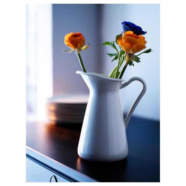 White enamel jug-shaped vase with orange flowers on a table.