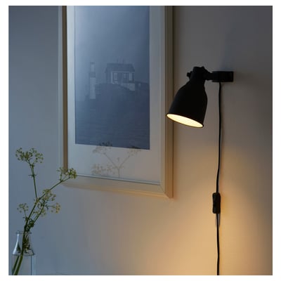 Wall-mounted black lamp illuminates a framed coastal art print next to a vase with flowers.