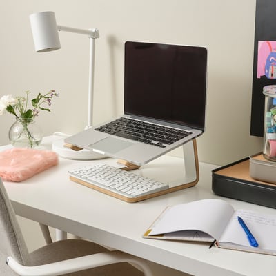 Laptop stand with laptop, keyboard, mouse, notebook, pen, and flowers.