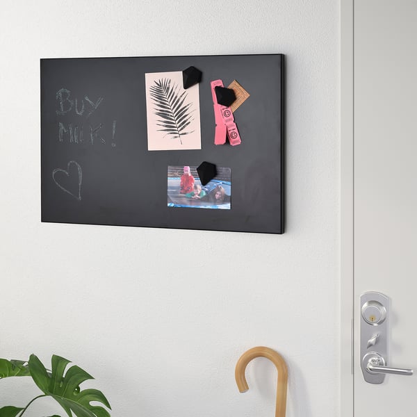 Black magnetic chalkboard on wall holds paper, photos, and notes. Used for reminders and decorations.