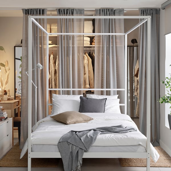 Modern white four-poster bed with sheer curtains in spacious room.
