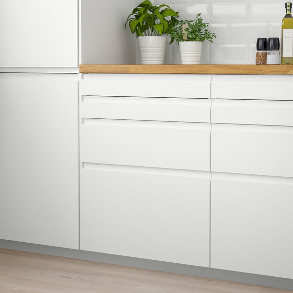 Modern white VOXTORP kitchen cabinets with integrated handles, sleek and minimalist design, smaller plants and items on top.