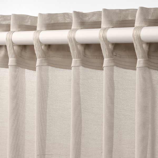 White rod with beige sheer curtains hanging, displaying gather tabs and allowing light through.