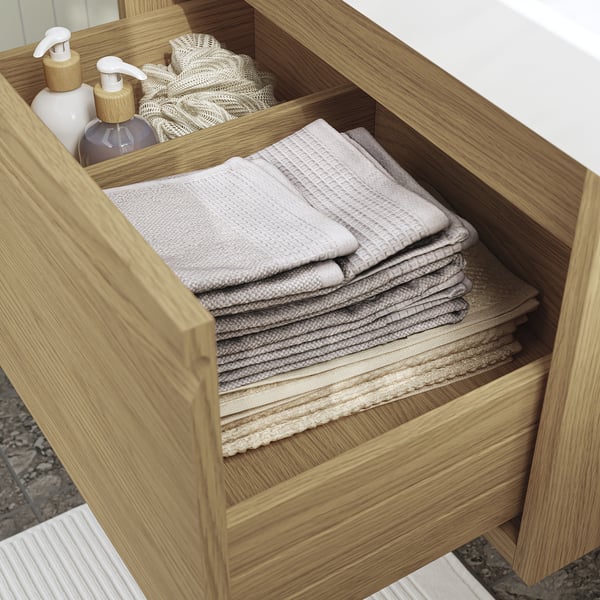 Wooden bathroom drawer with neatly folded towels and pump dispensers.