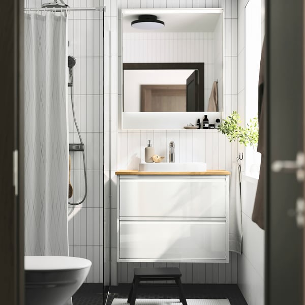Modern white ÄNGSJÖN bathroom with bamboo sink cabinet, space-saving wall mount, minimalist stool, glass shower & toilet.