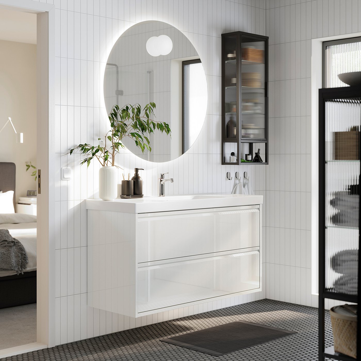 Modern bathroom scene: white ÄNGSJÖN vanity, round mirror, black accessories, plant. Space-saving design.