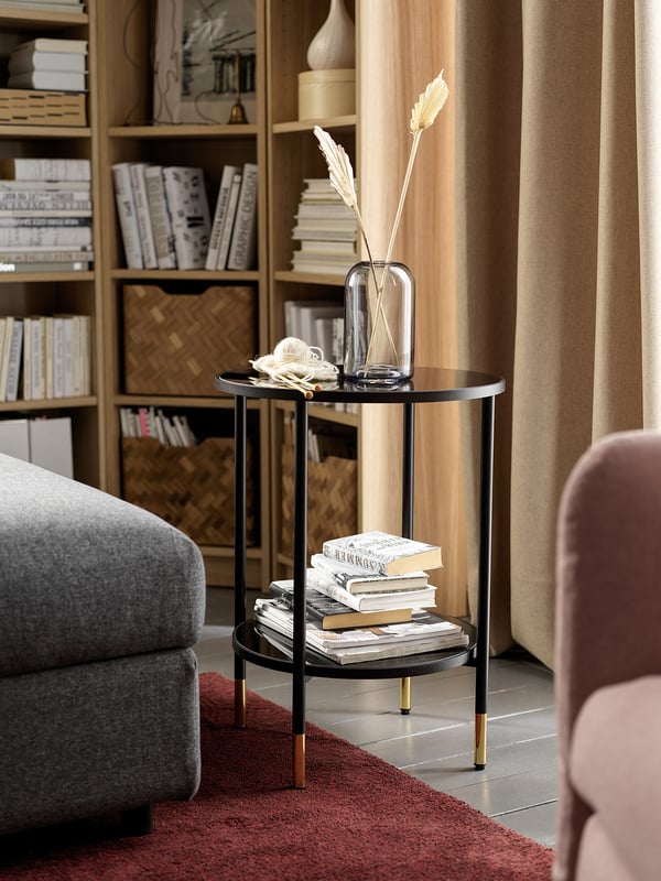 Modern living room with black ÄSPERÖD side table featuring smoky glass top, golden accents, and dried flowers in a clear vase.