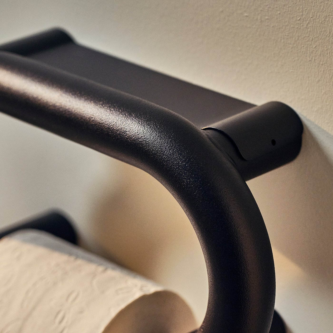 Black BÄSINGEN toilet roll holder in dark grey, wall-mounted, curved design with no visible screws.