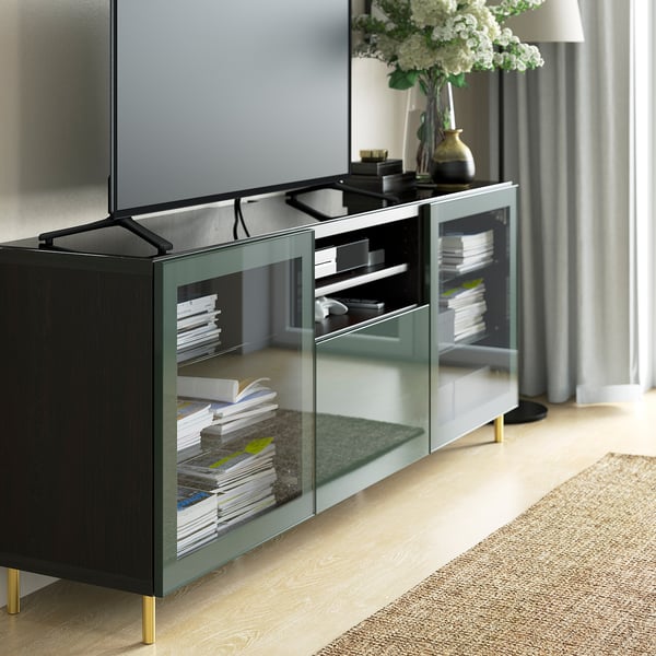 Contemporary living room with BESTÅ tv stand, glass top, mirrored doors, gold legs, books, and flat-screen tv on light wood floors.