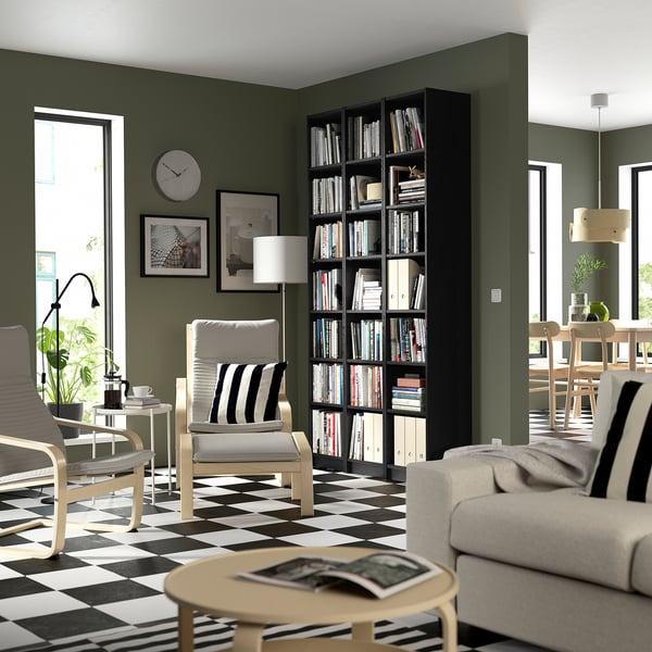 Modern living room with olive walls, BILLY black bookcase tall on right, white couch, striped floor, coffee table, and clock.