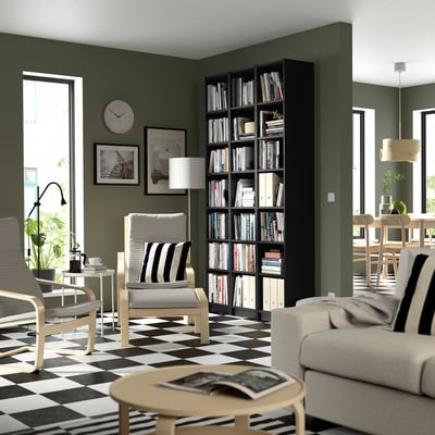 Modern living room with olive walls, BILLY black bookcase tall on right, white couch, striped floor, coffee table, and clock.