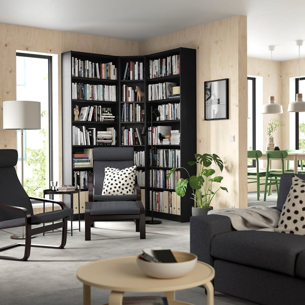 Modern living area with BILLY black bookcases, grey furniture, large windows, cosy seating, and green accents.