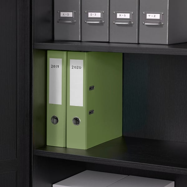 Black bookshelf with grey boxes labelled a-d, e-j, k-o, t-z on top, green binders labelled 2019 and 2020 below, and a grey box at bottom.