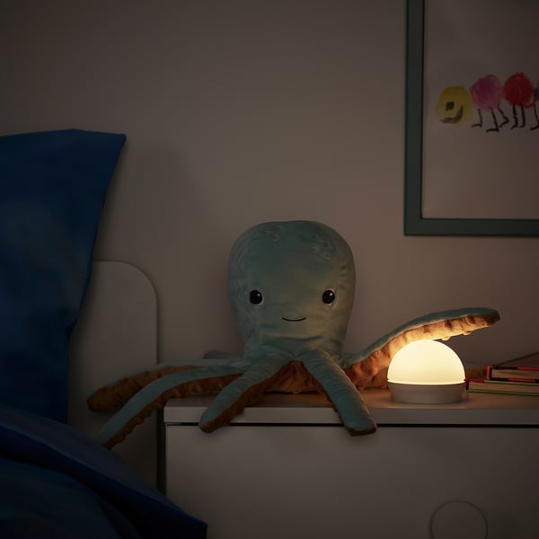A plush octopus lamp sits on a drawer, its head glowing softly. The warm light provides a gentle nightlight.