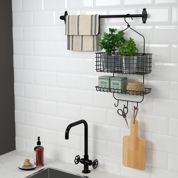 Modern kitchen with wall-mounted storage rack featuring hanging towels, plant, and kitchen tools. Black tap and white subway tiles visible.