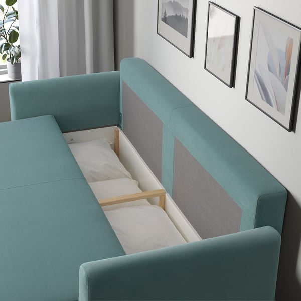 A teal sofa converts into a bed with under-seat bedding storage.