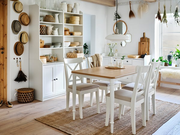 Cosy dining room with white DANDERYD table and chairs, oak top, steel legs, under soft pendant lights, near shelves with baskets, vases, and dishes.