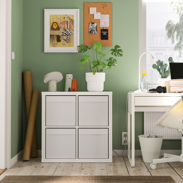 Small white DRÖNA storage box on shelf, holds items neatly. Bright green room with plants, art, and officespace.