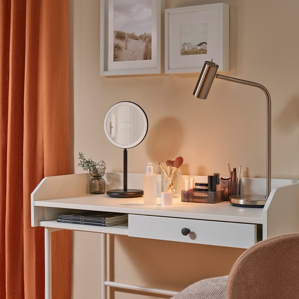 A modern vanity desk with a lit magnifying mirror, makeup, and decor.