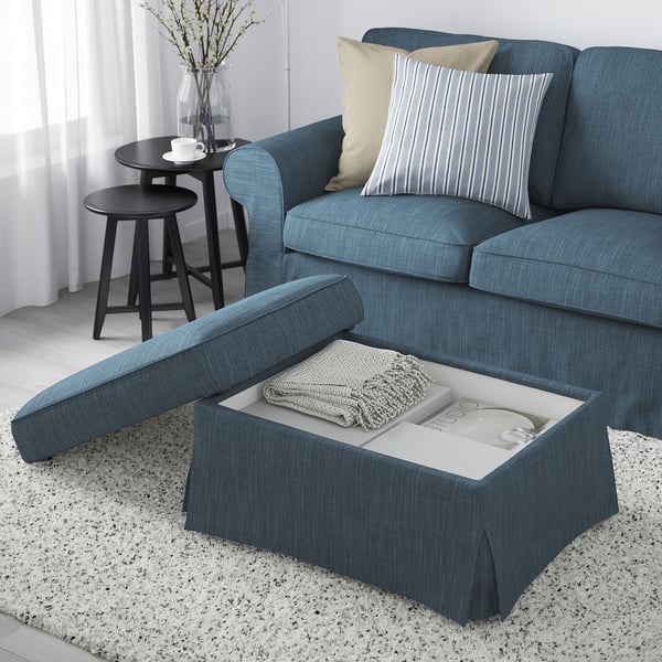 Blue sofa with footstool featuring hidden storage. Pillows, cup, and blanket displayed.